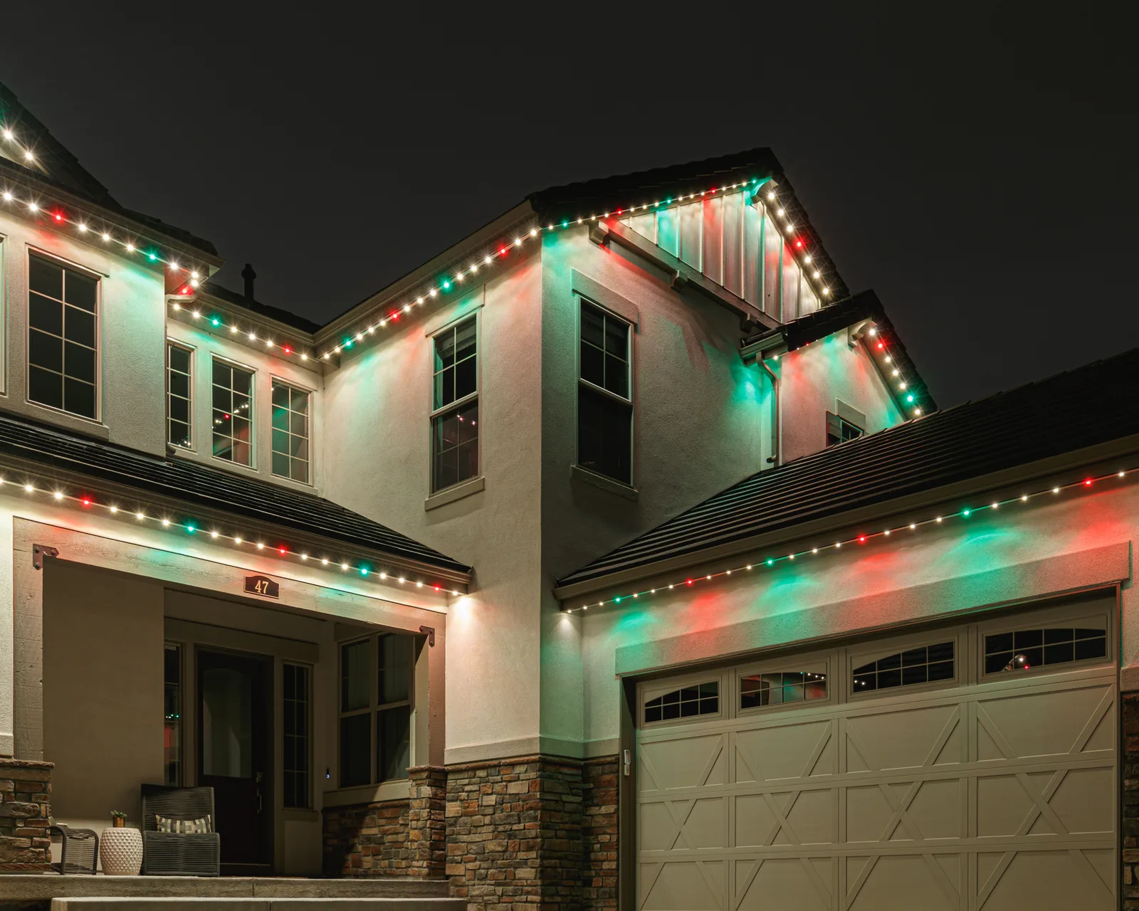 Two-story stucco home at night, Gemstone roofline pixels alternating red, green and warm white above the garage and front entry